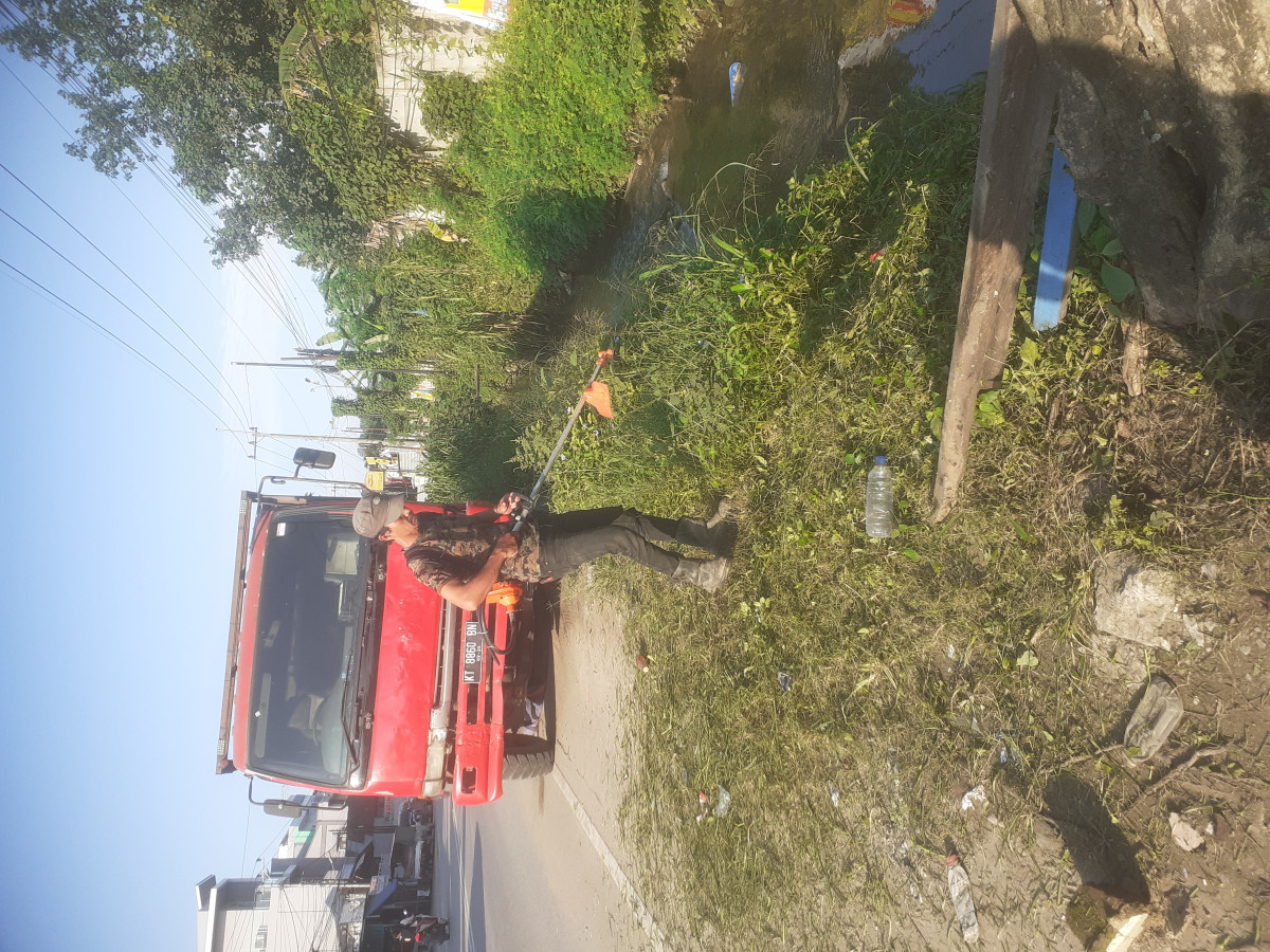 Kerja bakti membersihkan rumput di pinggir jalan di samping paret